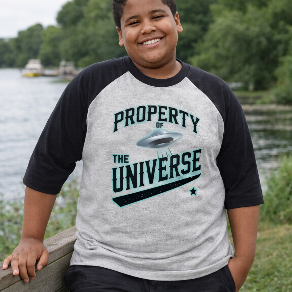Person wearing a 'Property of the Universe' t-shirt by a body of water.