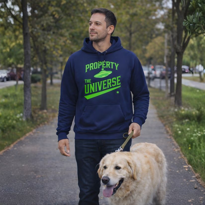 Man walking a dog on a path with a hoodie that says 'Property of the Universe' in a park-like setting.