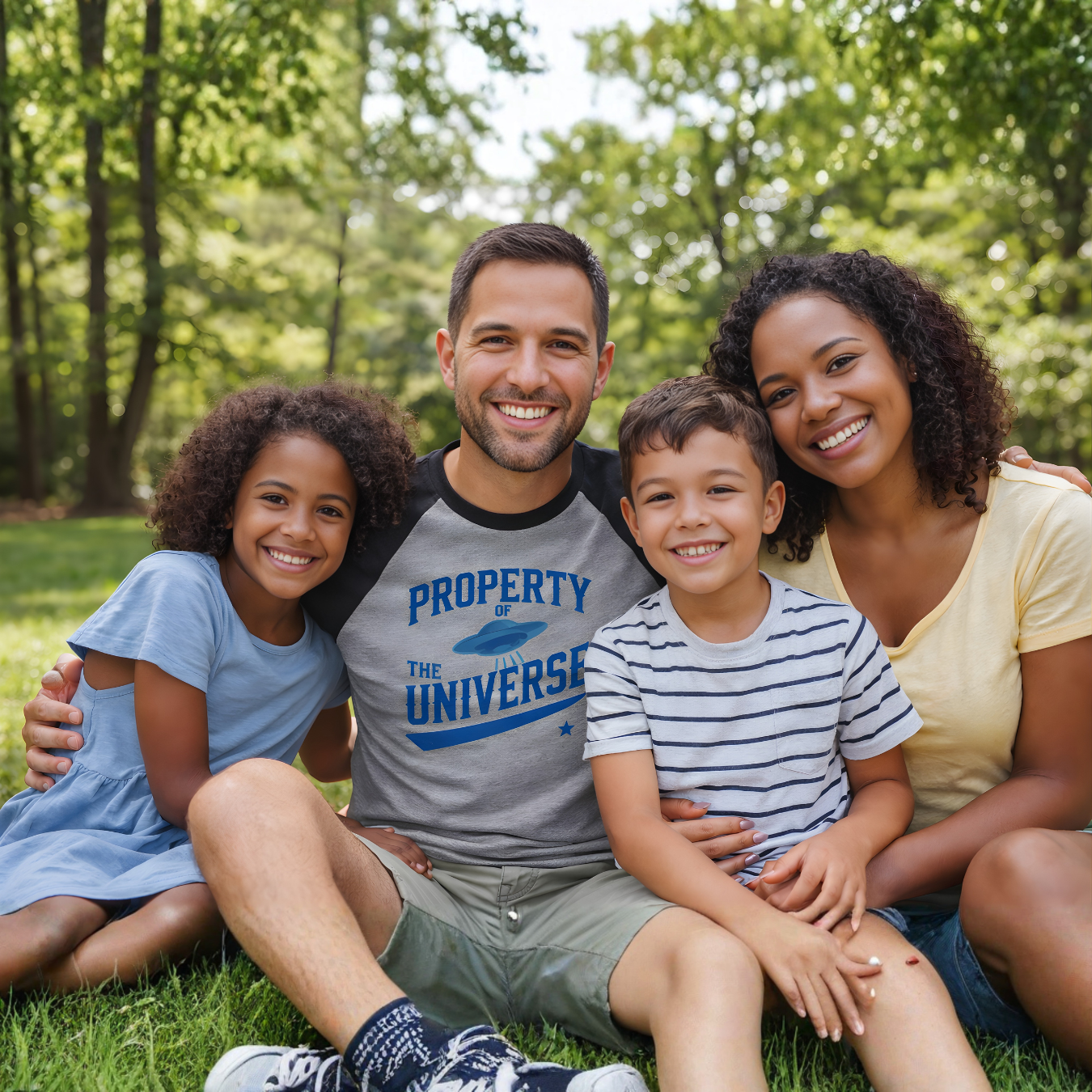 Family of four sitting on grass with trees in the background.