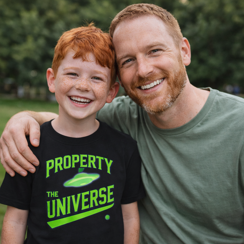 Man and child smiling together outdoors, with the child wearing a shirt that says 'Property of the Universe'.