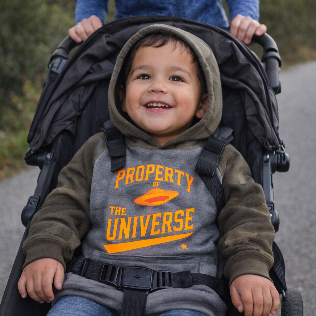 Child in a stroller wearing a hoodie with 'Property of the Universe' text